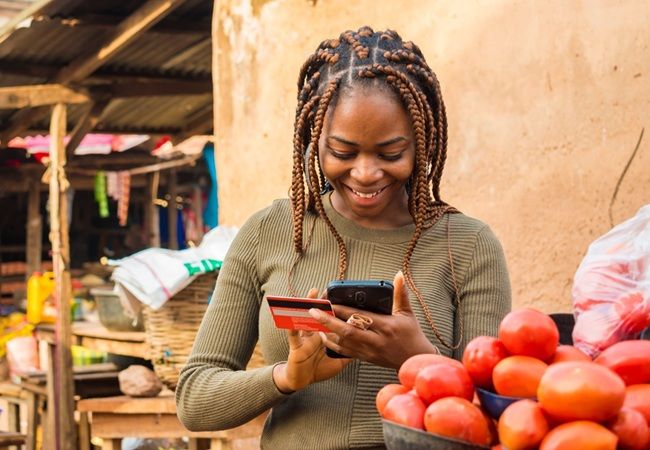 young african woman selling in a local african market using her mobile phone and credit card to do a transaction online